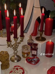 a table topped with lots of red candles and other items next to a mirror on top of a counter