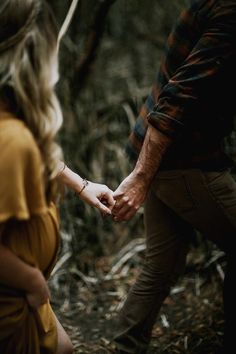 a couple holding hands while walking through the woods