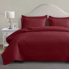 a bed with red comforter and pillows in a room next to a white headboard