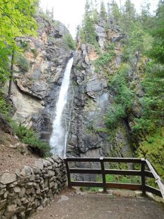 a large waterfall is coming down the side of a mountain in front of a wooden fence