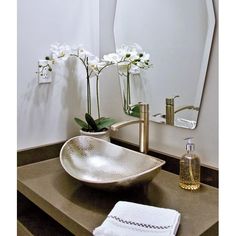 a bathroom sink sitting under a mirror next to a vase with white flowers in it