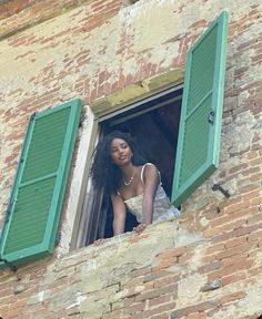 a woman is looking out the window of an old brick building with green shutters