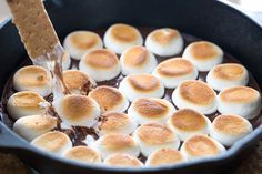 a skillet with marshmallows and chocolate sauce being stirred by a spatula