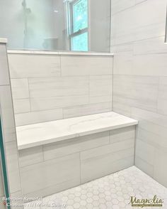 a white bathroom with hexagonal tile and glass shower door, along with a bench in the corner