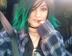 a woman with green hair sitting in the back seat of a car wearing a black and white checkered shirt