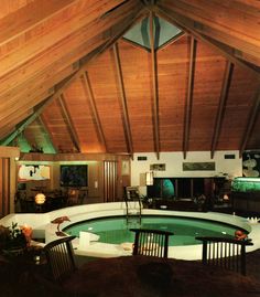 an indoor swimming pool in the middle of a room with wood ceilinging and wooden chairs