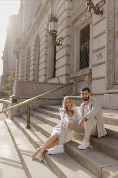 a man and woman sitting on the steps in front of an old building, posing for a photo