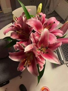 a bouquet of pink lilies sitting on top of a table next to a laptop