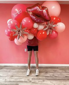 a person standing in front of a pink wall with balloons and lipstick on the lips