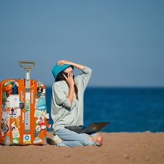 a woman sitting on the beach next to an orange suitcase