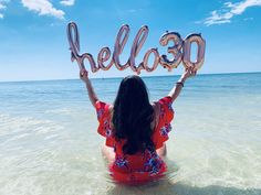 a woman sitting in the ocean holding up balloons that spell out hello - 350 on her head