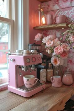 a pink coffee machine sitting on top of a wooden counter next to a vase with flowers