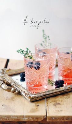 three glasses with blackberries and mint garnish sit on a tray next to some silverware