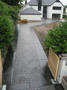 a brick walkway leading to a house with trees in the back ground and bushes on either side