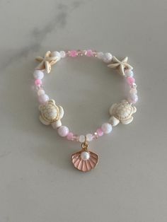 Pink Beach themed bracelet with turtle and starfish beads plus a shell charm with a pearl. Includes an assortment of beautiful light pink beads that looks like a sunset. Elastic band that fits any sized wrist making it perfect for anyone! Mermaid Pearl Jewelry, Bracelet Beach Summer, Cheap Beaded Bracelets With Heart Beads For Beach, Beach Theme Bracelets, Sea Shell Bracelet Diy, Beaded Bracelets Beach, Pink Starfish Jewelry For Gift, Beach Pearl Bracelet With Round Beads And Charm, Adjustable Starfish Bracelet With Lobster Clasp