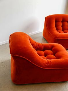 two orange chairs sitting next to each other on the floor in front of a white wall