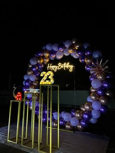 a large purple and gold balloon arch with the number twenty two on it at night