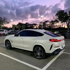 a white bmw suv parked in a parking lot at dusk with the sun going down