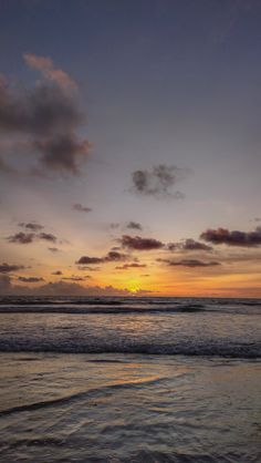 the sun is setting over the ocean with clouds in the sky and waves on the beach