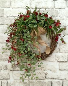 a wreath with red berries and green leaves hanging on a brick wall