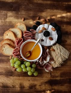 an assortment of food including bread, grapes and nuts on a wooden table with wine