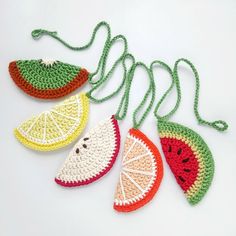 four crocheted slices of fruit are hanging from a string on a white surface