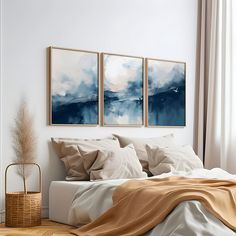 two paintings on the wall above a bed in a room with wood flooring and white walls