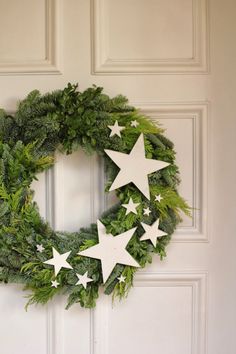 a green wreath with white stars hanging on the front door to decorate it for christmas