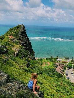 a woman sitting on top of a lush green hillside next to the ocean and beach