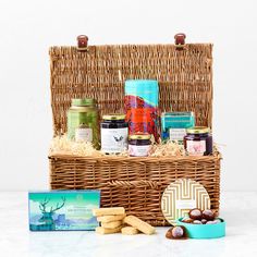 a wicker basket filled with cookies, jams and crackers next to a box of biscuits