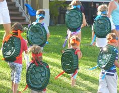 several children with backpacks that look like turtle turtles are walking in the grass together