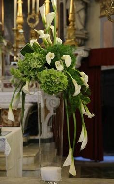 a vase filled with white flowers and greenery on top of a table next to a chandelier