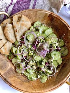 a wooden bowl filled with cucumber and red onion salad next to crackers