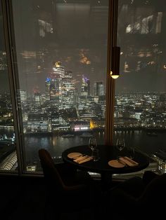 two chairs and a table in front of a large window overlooking the city at night