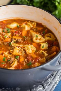 a pot filled with pasta and meat soup on top of a blue cloth covered table