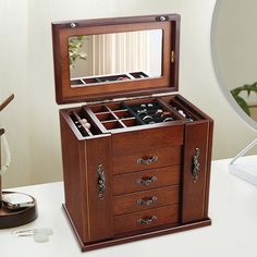 an open wooden jewelry box sitting on top of a white table next to a mirror