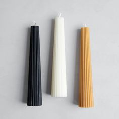 three candles sitting next to each other on top of a white surface, one black and one orange