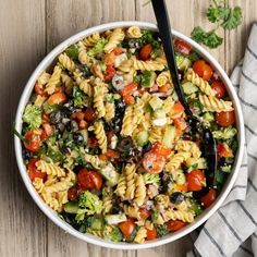 a white bowl filled with pasta salad on top of a wooden table next to a napkin