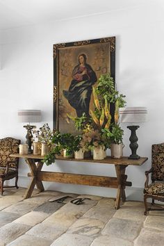 a painting hangs on the wall above a table with potted plants and other decorations