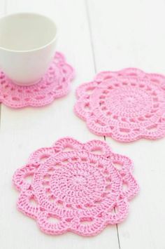 crocheted coasters are sitting next to a cup on a white wooden table