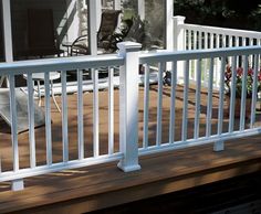 a porch with white railings and chairs on the front deck, next to a house