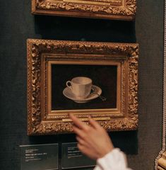 a person pointing at a painting on display in front of other framed art pieces and paintings