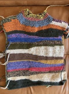 a crocheted sweater sitting on top of a brown leather couch next to a pair of scissors