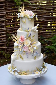 a three tiered white cake with flowers on it's side and birds on top