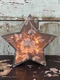 a lighted star with flowers on it sitting on top of a wooden table next to a wall