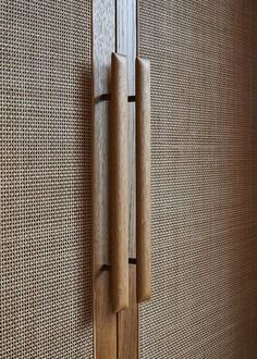 a wooden door handle on the side of a wall with woven fabric behind it,