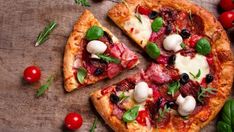 a pizza with various toppings on it sitting on a wooden table next to tomatoes and herbs