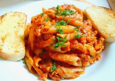 pasta and bread on a white plate with parsley sprinkled in tomato sauce