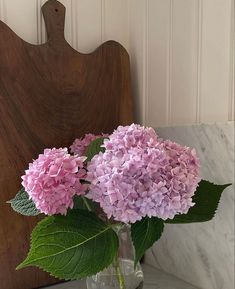 a vase filled with pink flowers sitting on top of a table next to a cutting board