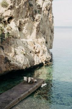 two chairs sitting on the edge of a cliff by the ocean with clear blue water